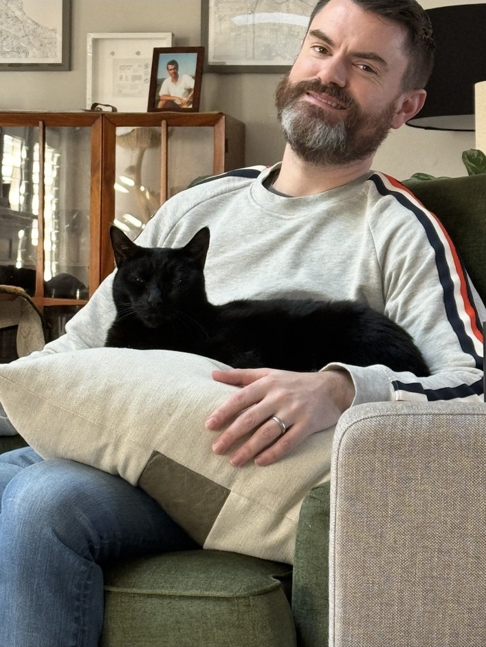 Johnny sitting in a chair with Bobby, a black cat, resting on his lap