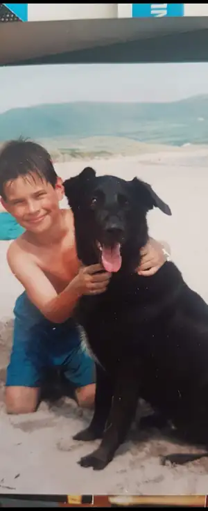 Micheal Sheehy as a child on a beach in Ireland with a black dog