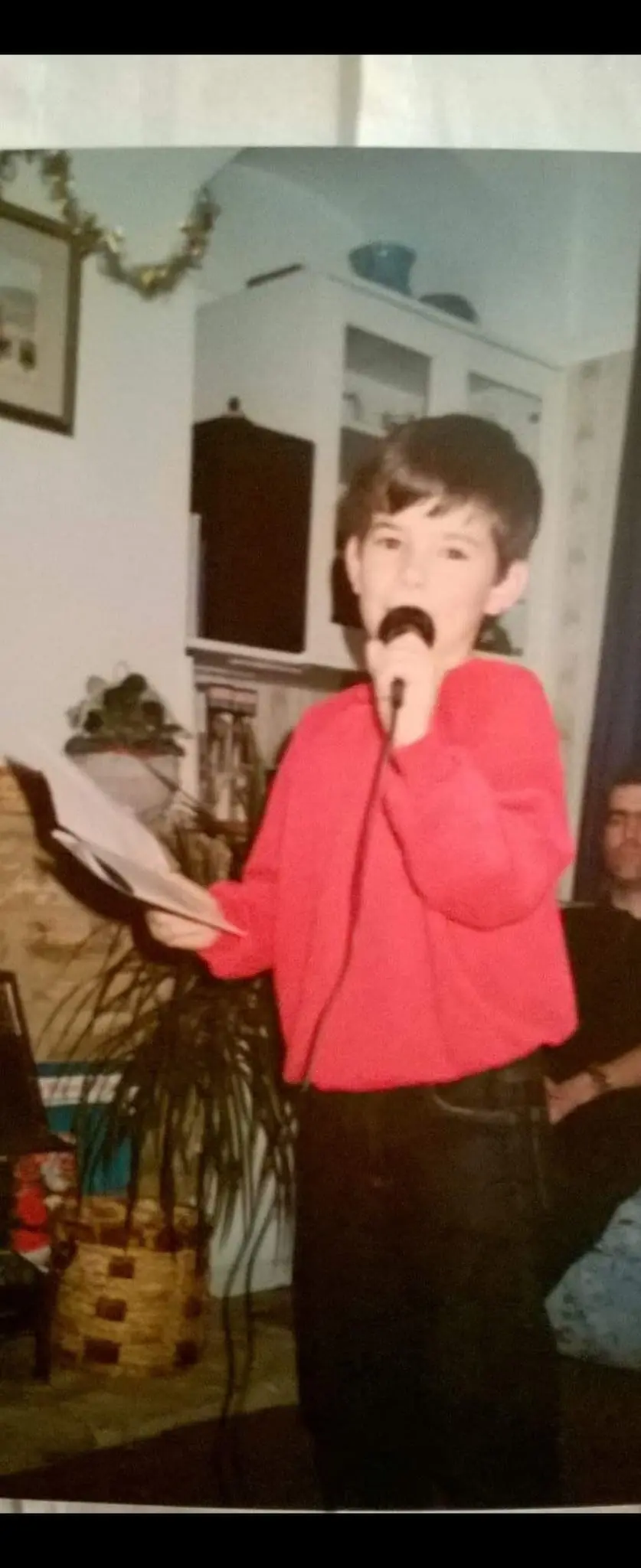 Micheal Sheehy as a child performing with a microphone and papers in hand